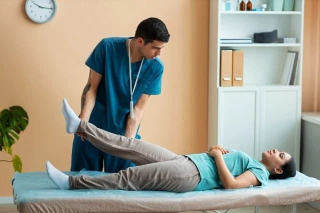 Physiotherapist assisting a patient with a leg exercise on a treatment table